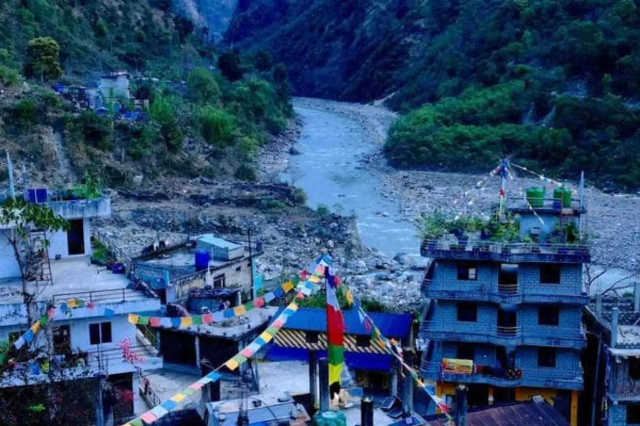 Colorful prayer flags strung across a riverside mountain village during Nepal trek tours.