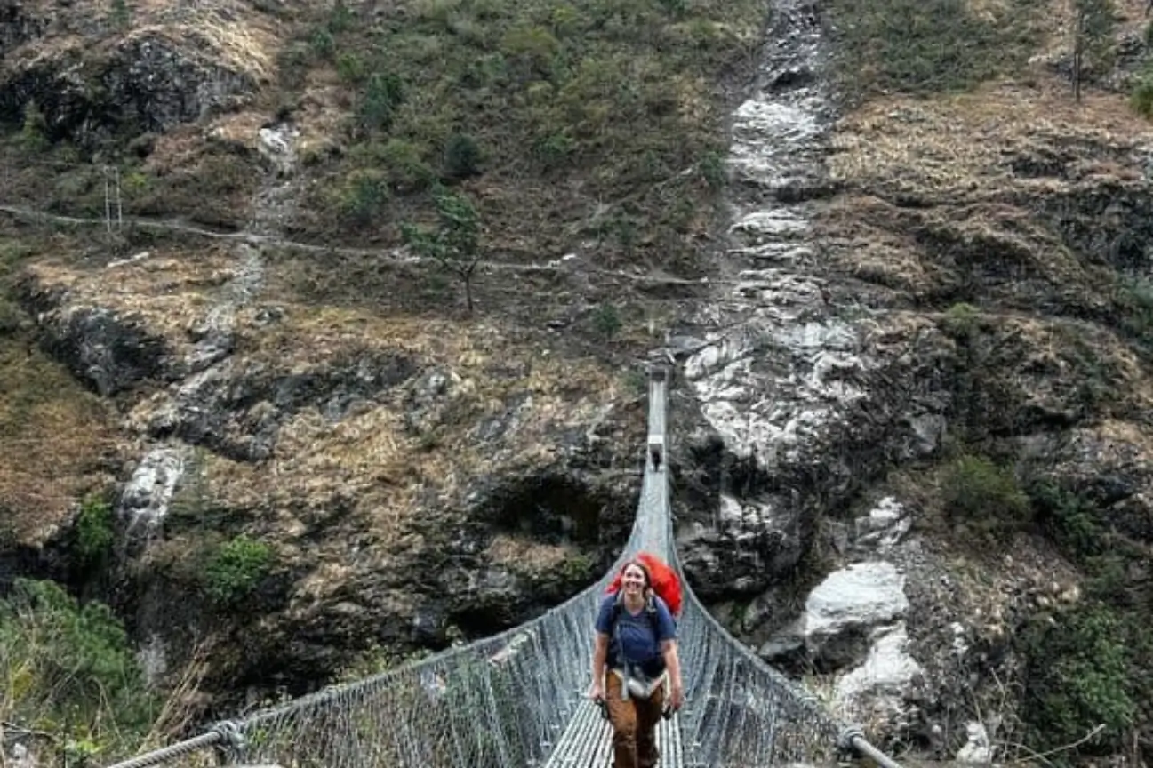 A trekker crossing a long suspension bridge surrounded by dramatic mountain terrain during Nepal trek tours.