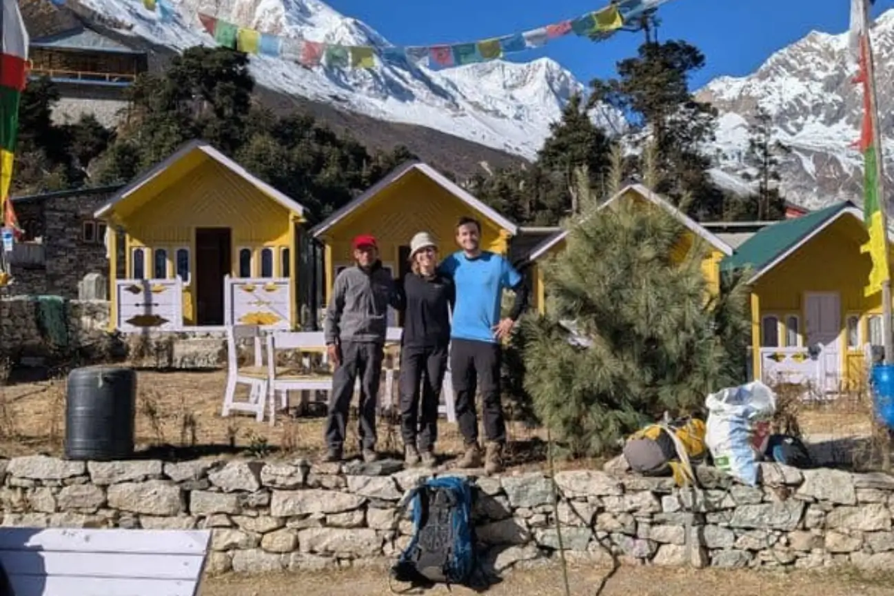 A happy couple posing outside charming yellow alpine lodges with snowy peaks during Nepal trek tours.